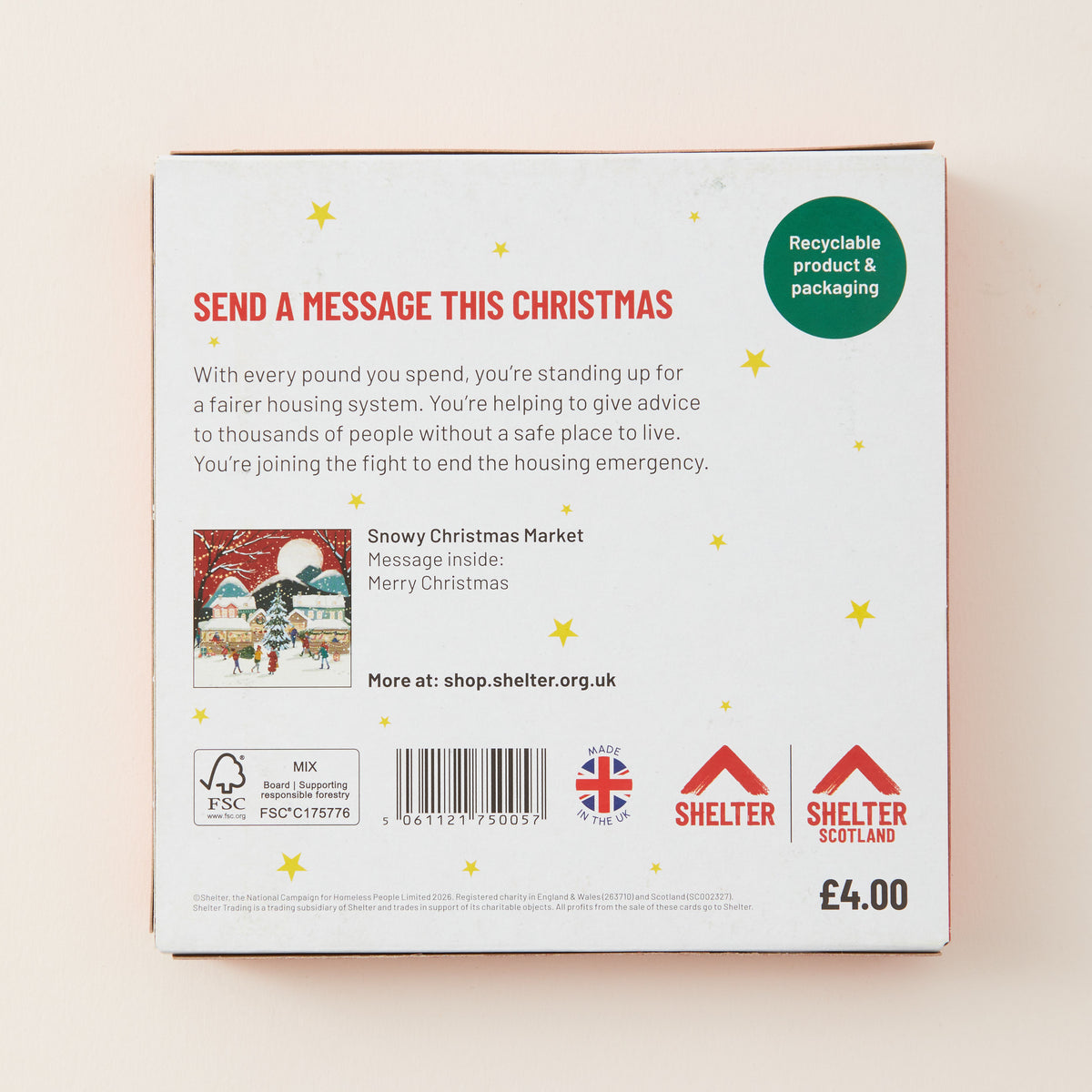 The back of a white Christmas message card box with red and black text, a small holiday illustration, a barcode, and Shelter branding, photographed against a light beige background.