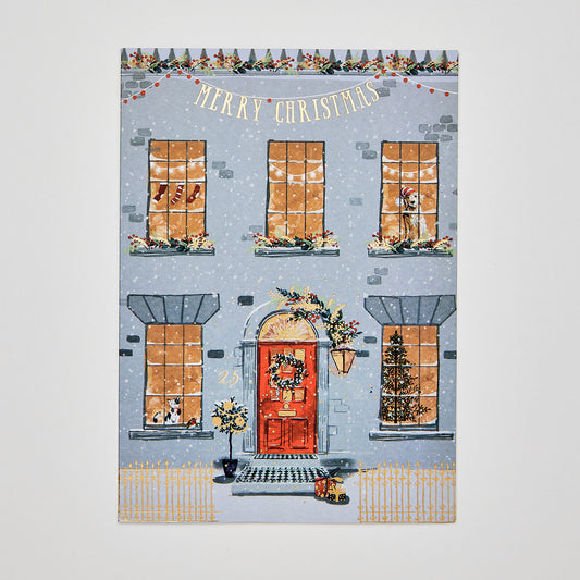 Flat lay of christmas card depicting a townhouse with festive decorations. Text reads 'merry christmas'