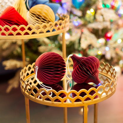 2 dark red hanging decorations on a nesting table with a christmas tree and lights in the background. Lifestyle image.