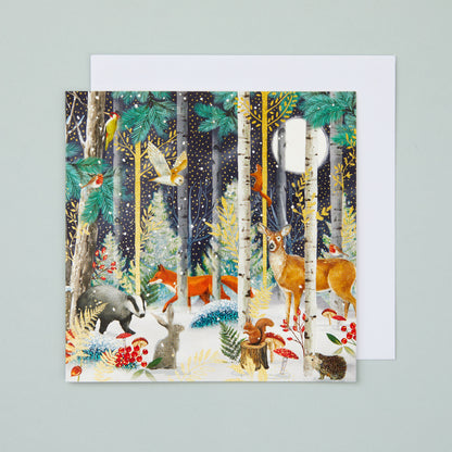 A square Christmas card with an illustration depicting a snowy night time forest scene with lots of  woodland animals. 