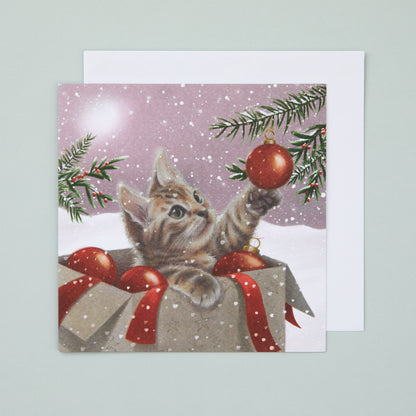 A square Christmas card with an illustration depicting a kitten pawing in a bauble on a Christmas tree. The kitten is sitting in the box of baubles and there is a snowy scene in the background.