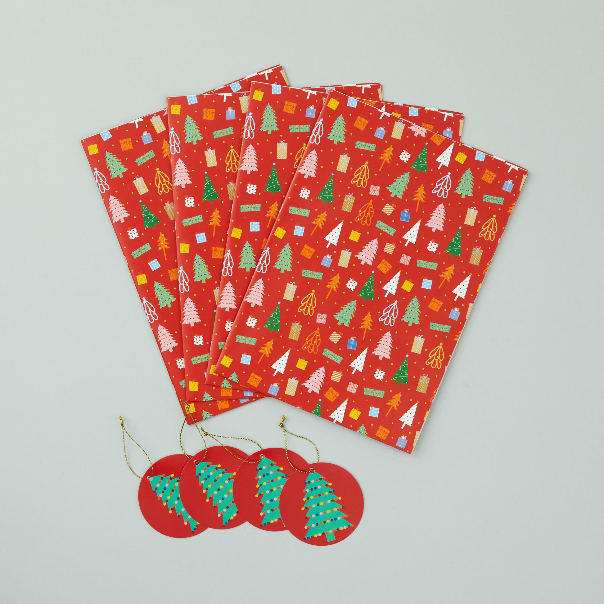 Four sheets of folded christmas trees wrapping paper with four matching gift tags.