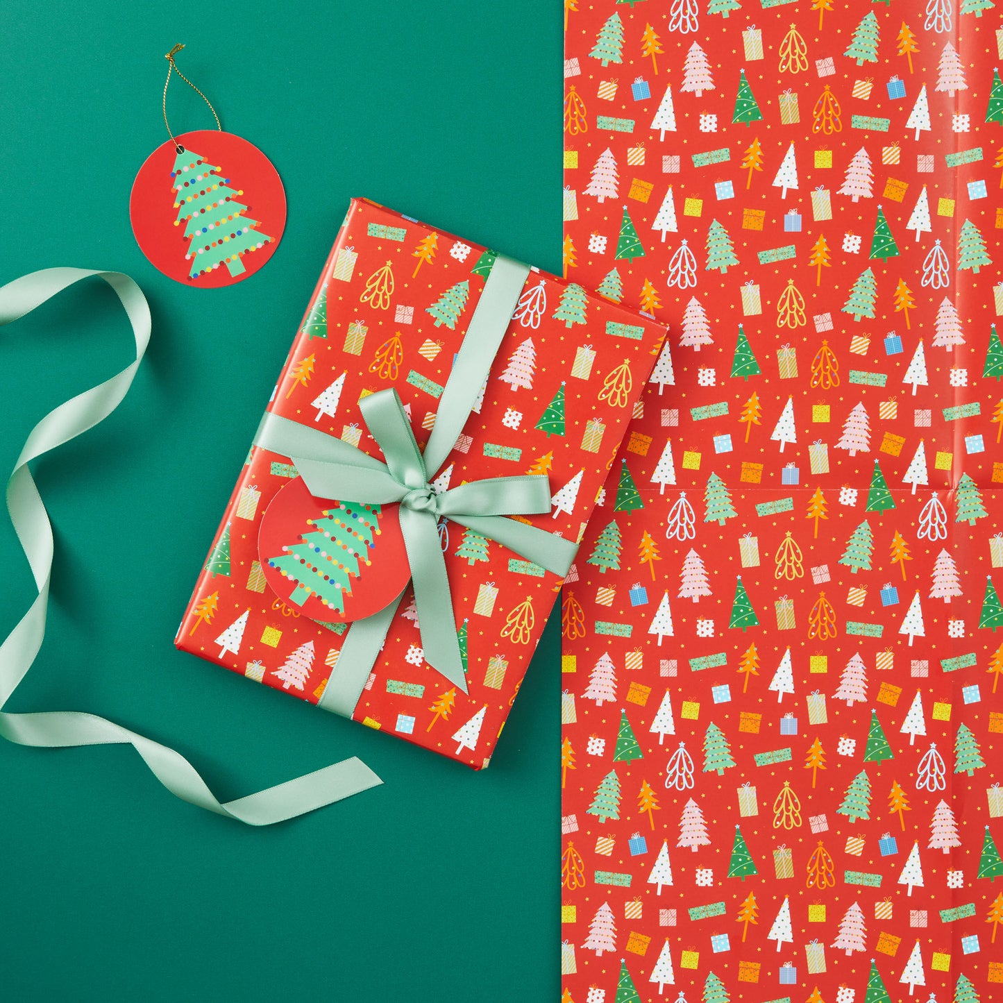 A present wrapped in 'Christmas Trees' wrapping paper tied with a light green ribbon.