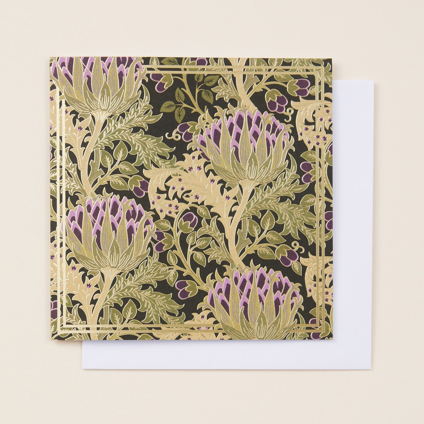 A square Christmas card with a pattern of gold and purple thistles on the front, sitting on a white envelope.