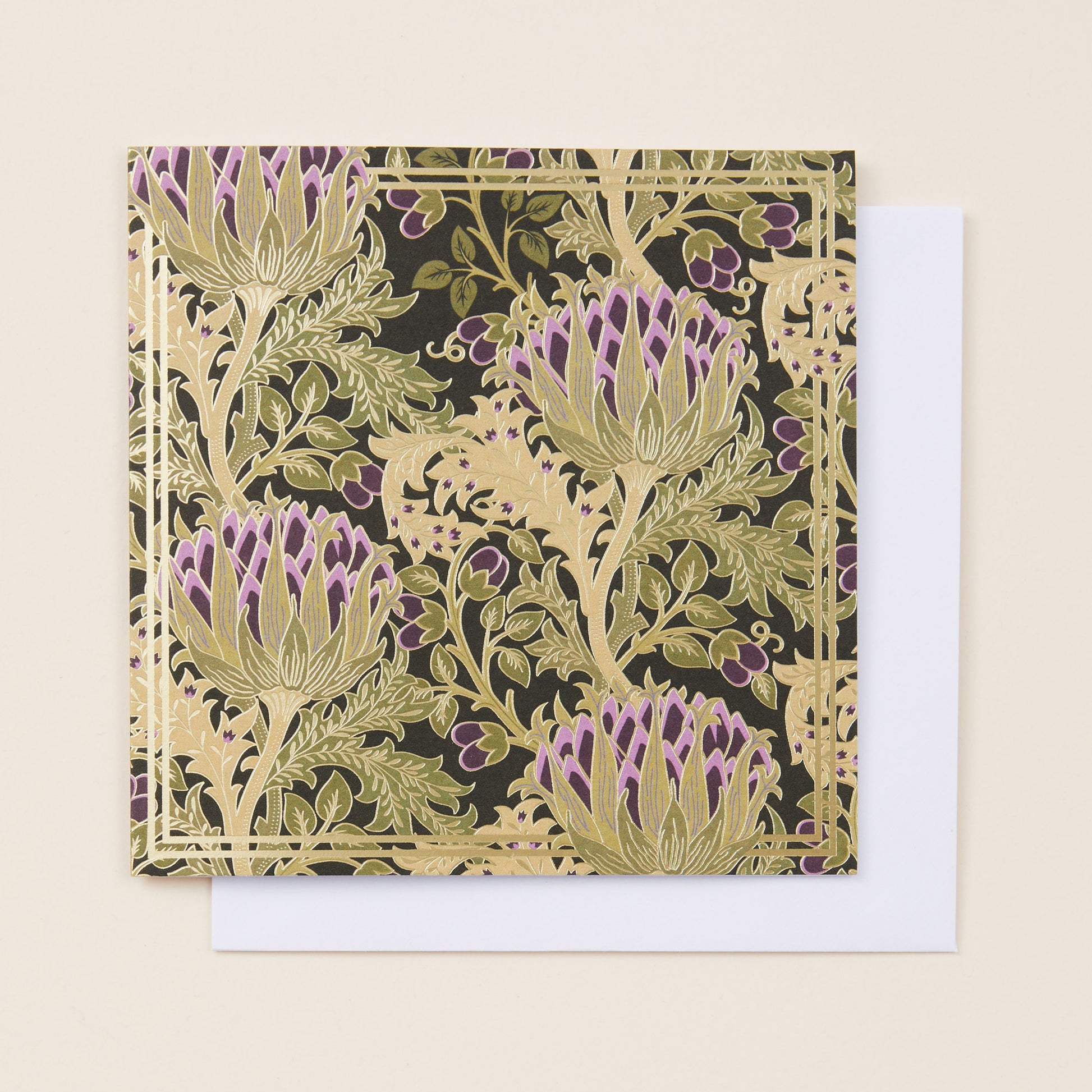 A square Christmas card with a pattern of gold and purple thistles on the front, sitting on a white envelope.