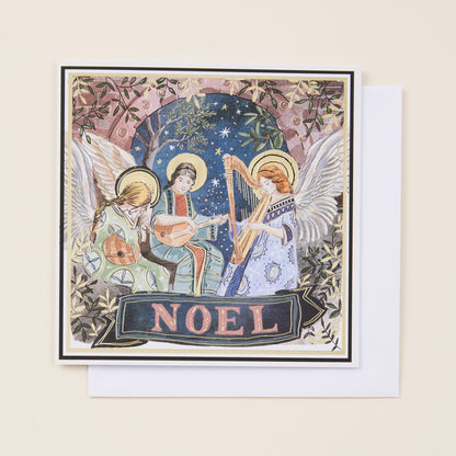 A square Christmas card with illustration of angels on the front, sitting on a white envelope.