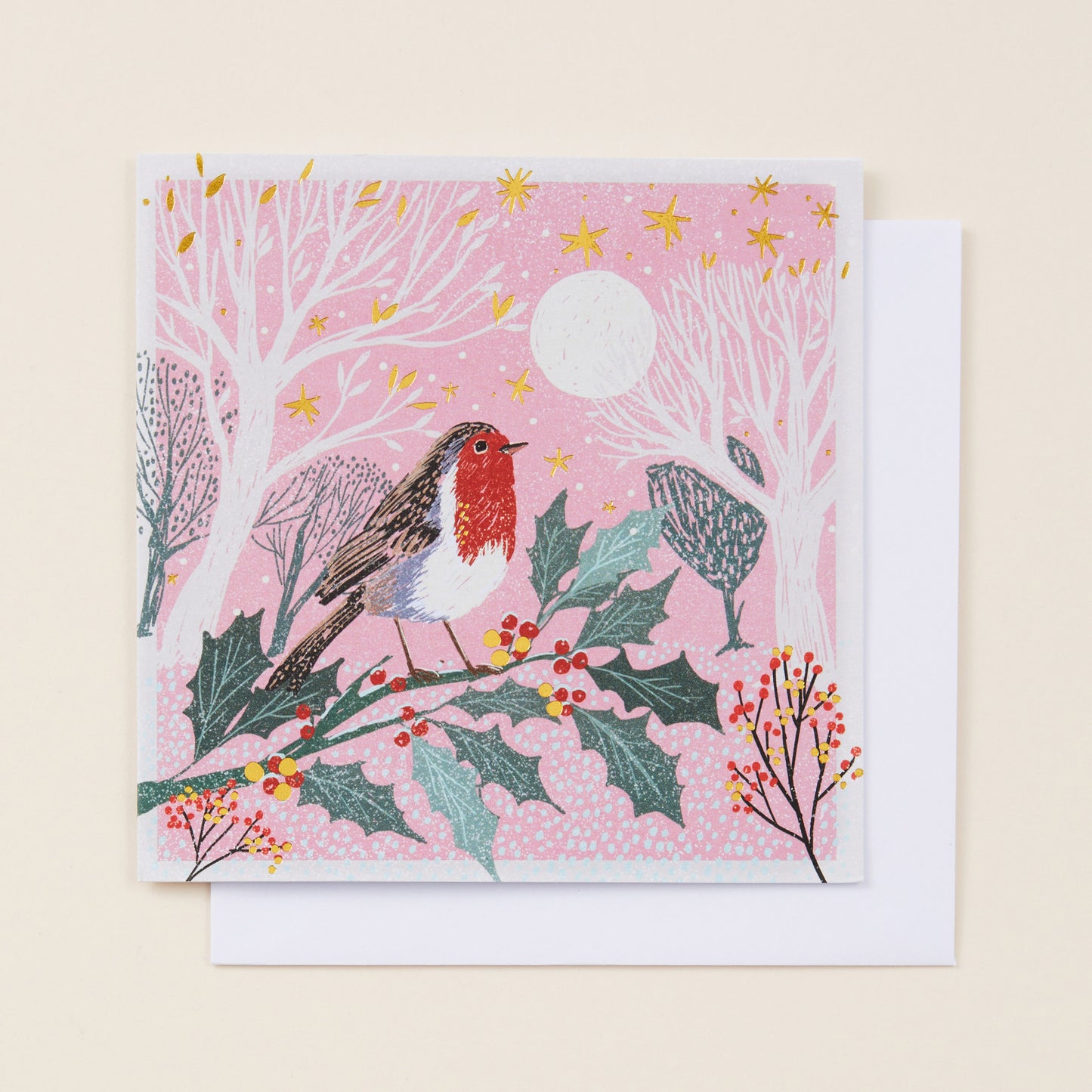 A square Christmas card with an image of a robin perched on a holly branch on the front of it, the card sitting on a white envelope.