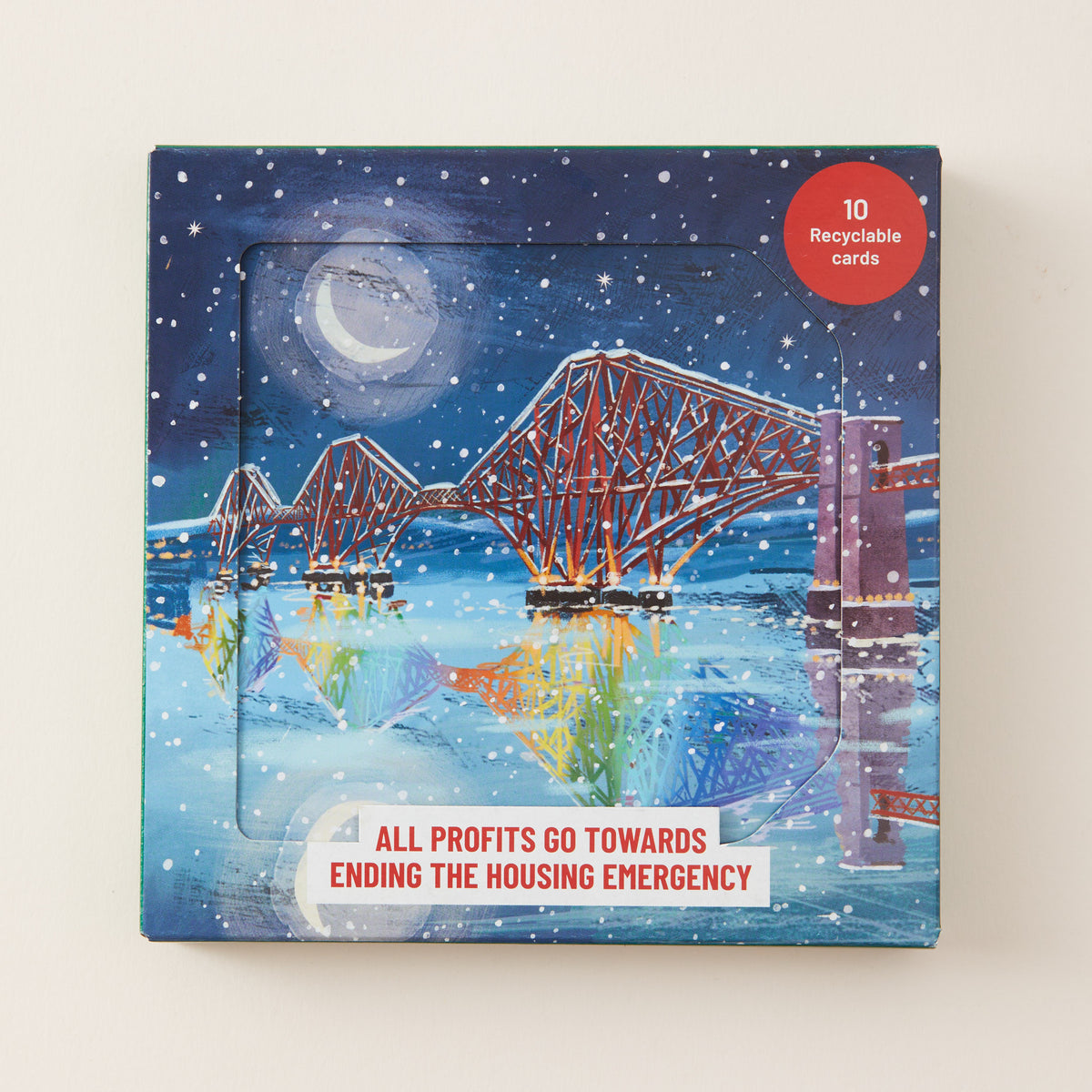 A square product box featuring a winter night scene with a depiction of the Forth Bridge over water under a moonlit sky. The box has a clear window showing cards inside, with text reading 'ALL PROFITS GO TOWARDS ENDING THE HOUSING EMERGENCY' and a red circle that says '10 Recyclable cards'.