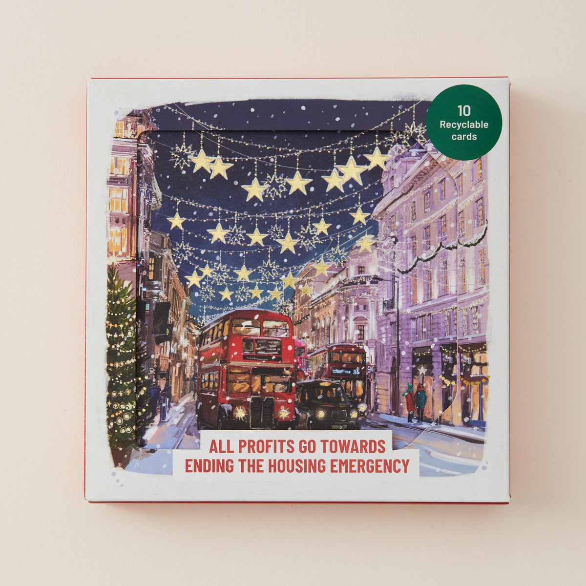 A square printed card or booklet cover shown against a light beige background. The front features an illustrated winter city street scene with red double-decker buses, buildings, hanging star lights, and a Christmas tree.