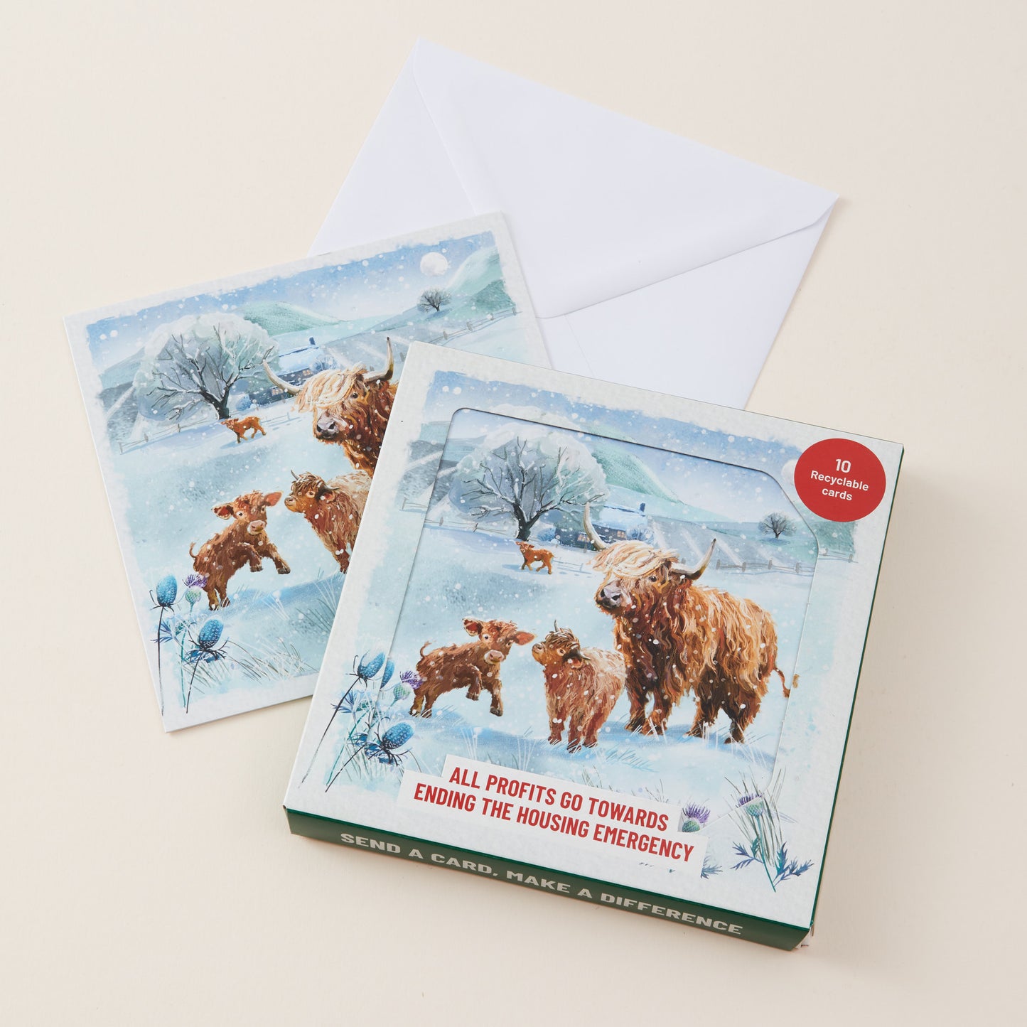 A boxed set of winter-themed cards and envelopes shown on a light beige background. The front card box features an illustration of Highland cows and calves in a snowy landscape.