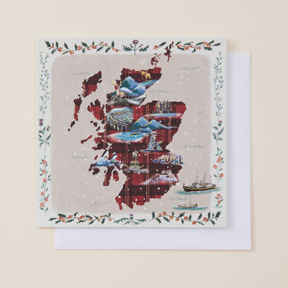 A square greeting card featuring a collage-style map of Scotland in red, blue, and gray tones, surrounded by a decorative holly and floral border, with a white envelope behind it on a light beige background.