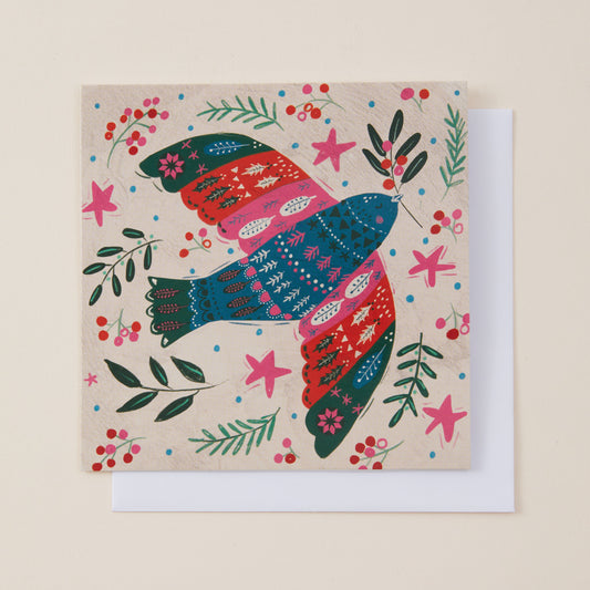 A square greeting card featuring a colorful, folk-art style bird with patterned wings, surrounded by green leaves, red berries, and pink stars on a beige background. A white envelope is partially visible behind the card.
