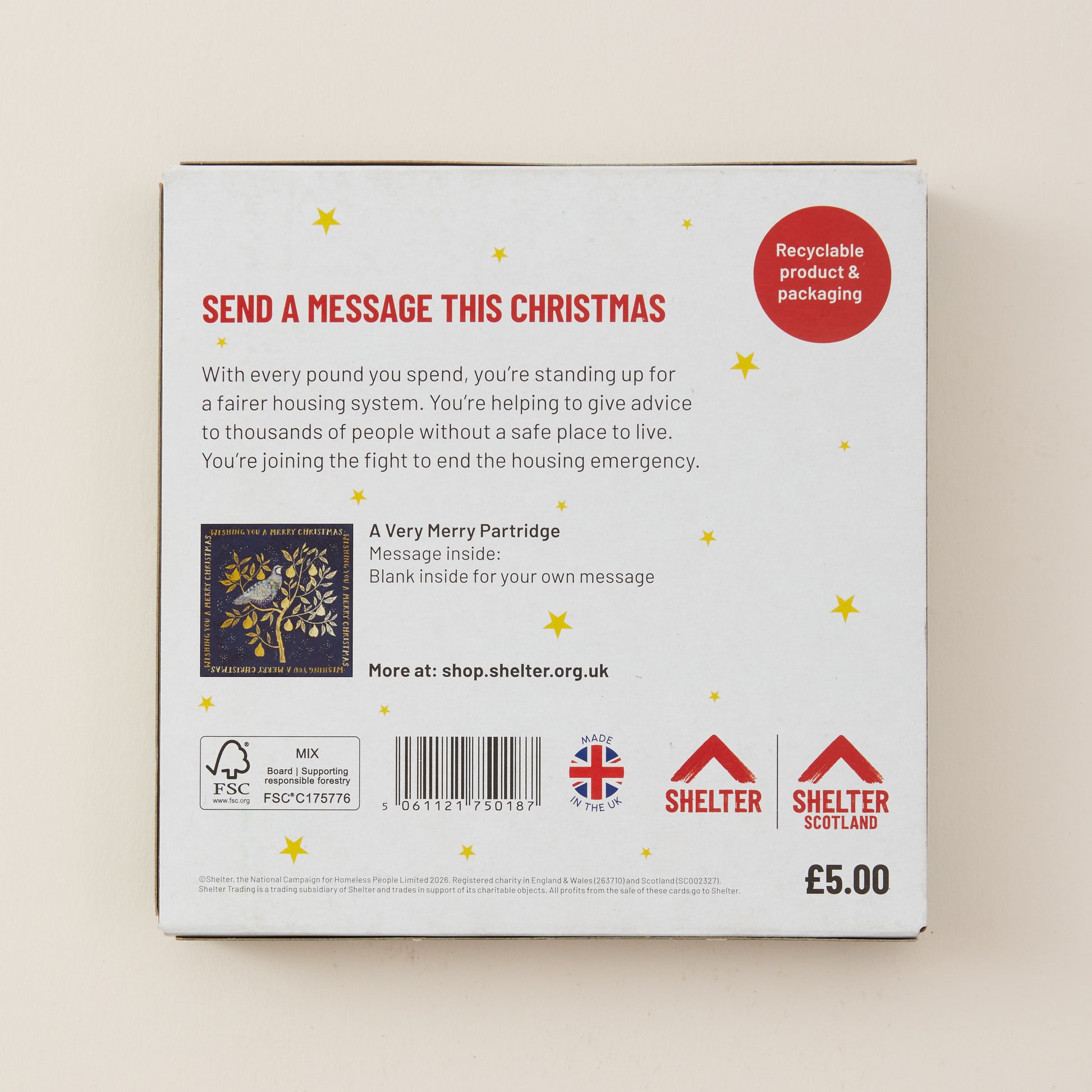 The back of a white cardboard box for Shelter UK, featuring red and black text, a Christmas-themed message, a barcode, and recycling and UK logos, photographed against a light beige background.
