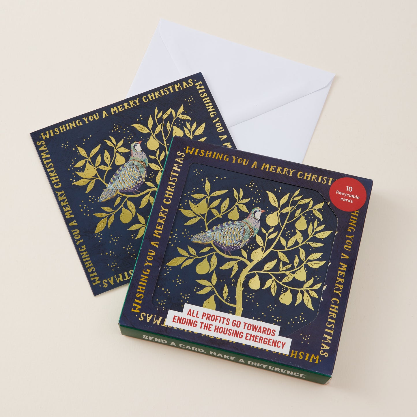 A boxed card set and two individual greeting cards are arranged on a light beige background. The cards have a dark navy blue background with metallic gold illustrations of a bird perched on a leafy branch, surrounded by gold text reading 'Wishing you a merry Christmas.