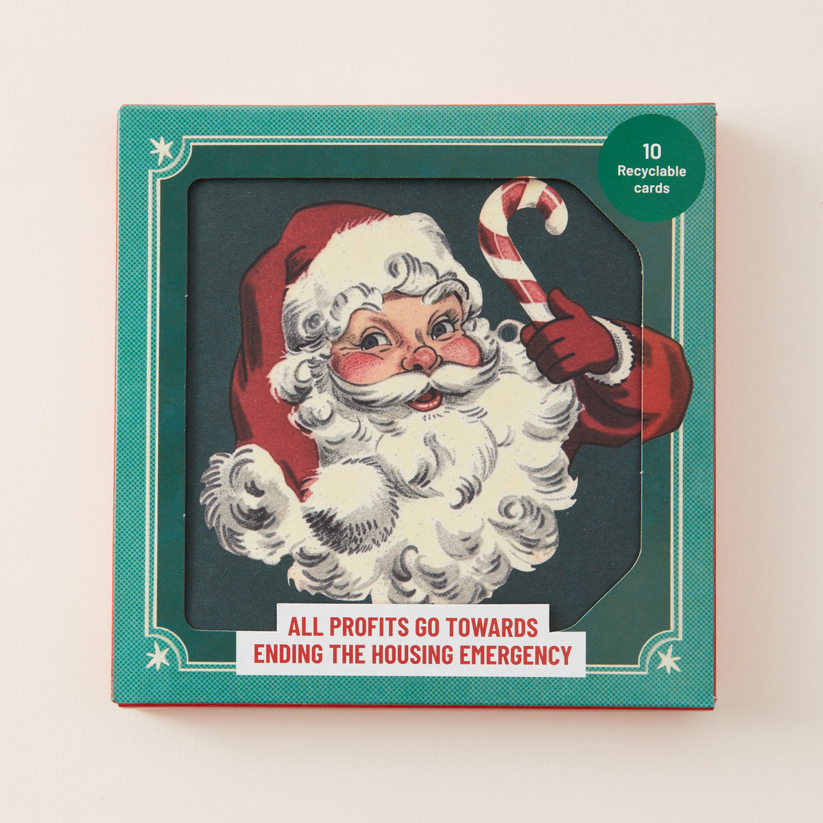 A square Christmas-themed card box with a teal border and a vintage-style illustration of Santa Claus holding a candy cane. The front reads 'ALL PROFITS GO TOWARDS ENDING THE HOUSING EMERGENCY' and has a green circle that says '10 Recyclable cards'.