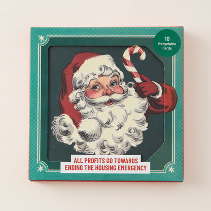 A square Christmas-themed card box with a teal border and a vintage-style illustration of Santa Claus holding a candy cane. The front reads 'ALL PROFITS GO TOWARDS ENDING THE HOUSING EMERGENCY' and has a green circle that says '10 Recyclable cards'.