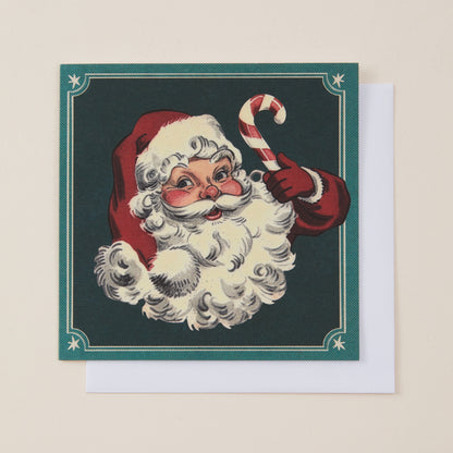 A square Christmas greeting card featuring a vintage-style illustration of Santa Claus with a white beard, red hat, and candy cane, shown with a white envelope behind it on a light beige background.