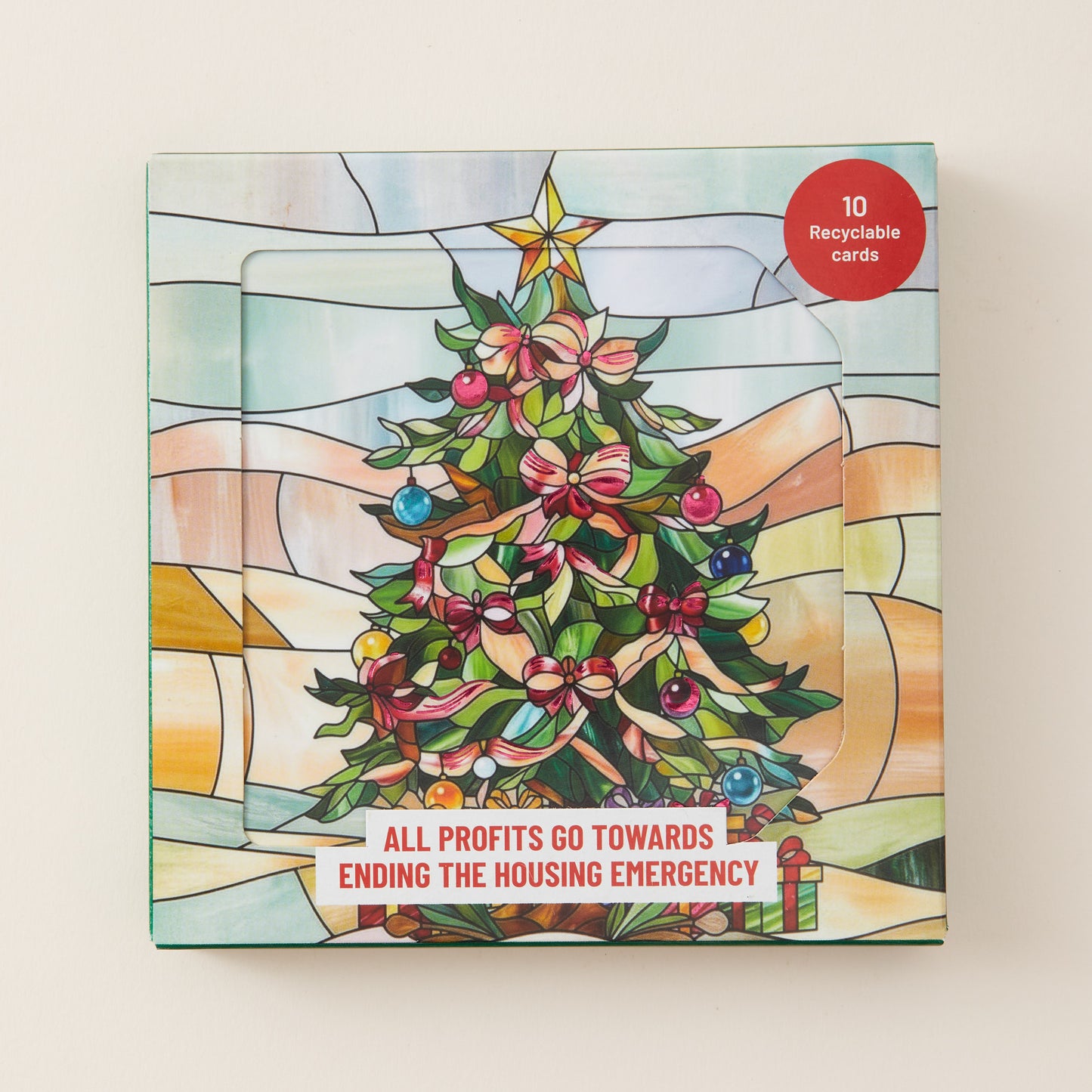 A square Christmas-themed card set box with a stained-glass style illustration of a decorated tree, a gold star, and a red circular badge that says '10 Recyclable cards.' The front also reads, 'ALL PROFITS GO TOWARDS ENDING THE HOUSING EMERGENCY.