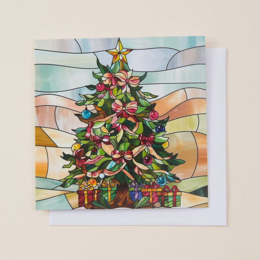 A square Christmas greeting card with a stained-glass style illustration of a decorated tree, shown with a white envelope on a light beige background.