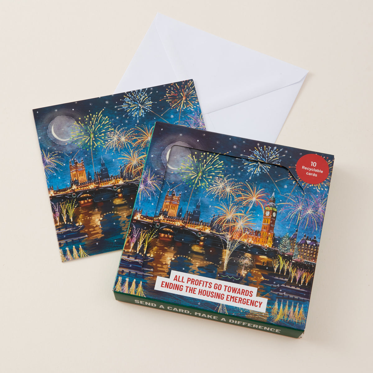 A boxed Christmas card set with two illustrated cards and a white envelope on a light beige background. The front box shows a nighttime London cityscape with fireworks.