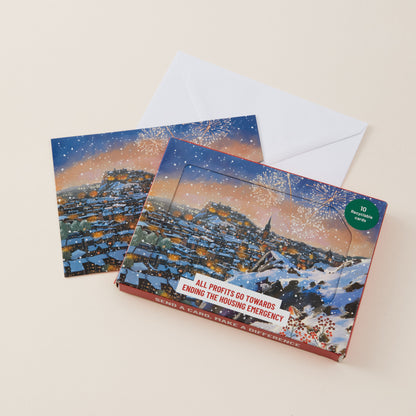 A holiday greeting card and matching envelope on a warm beige background. The card features a snowy view from Arthur's Seat in Edinburgh and a green circular badge that reads '10 CARDS TO END THE HOUSING EMERGENCY'.