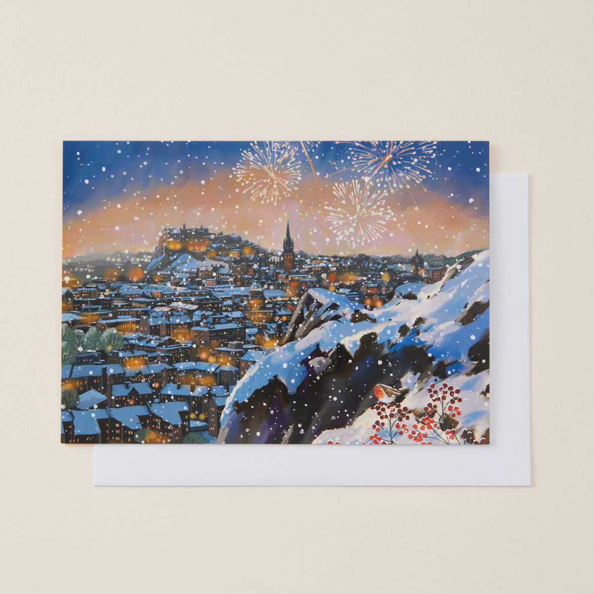 A square art print or greeting card showing a snowy hillside view from Arthur's Seat in Edinburgh, displayed against a plain light beige background with a white envelope behind it.