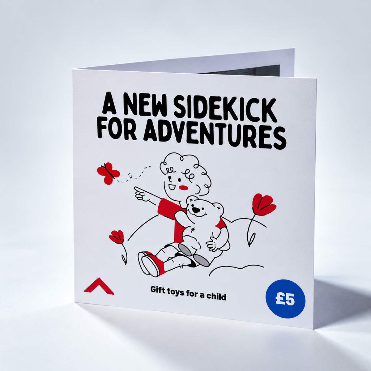 A folded white gift card or gift box cover standing upright on a light gray studio background. The front reads 'A NEW SIDEKICK FOR ADVENTURES' in large black text, with a simple line drawing of a child and bear in red, black, and white, plus a blue circle that says '£5'.