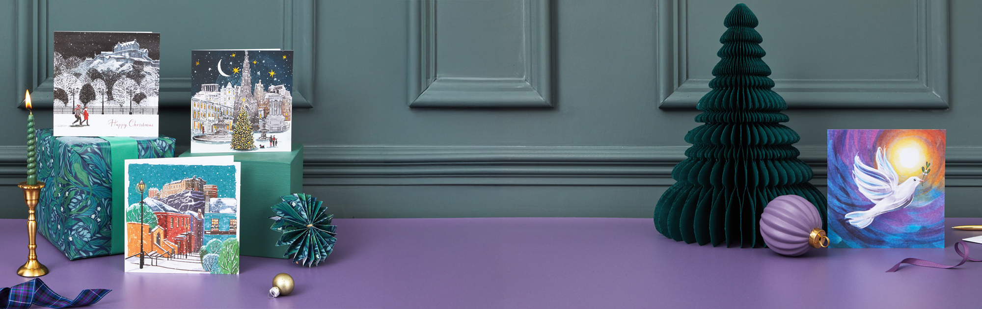 Collection of Christmas cards and decorations on a purple surface with a green wall.