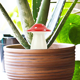 A photo of a ceramic white and red mushroom sitting in a plant pot.