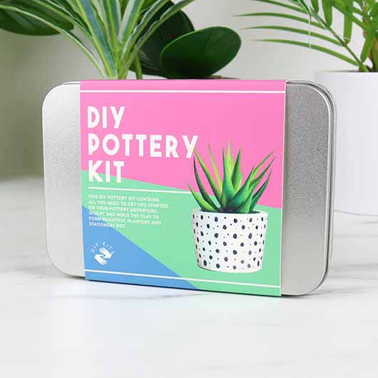 A silver tin sitting on a white table with a cardboard sleeve round it that reads 'DIY POTTERY KIT'