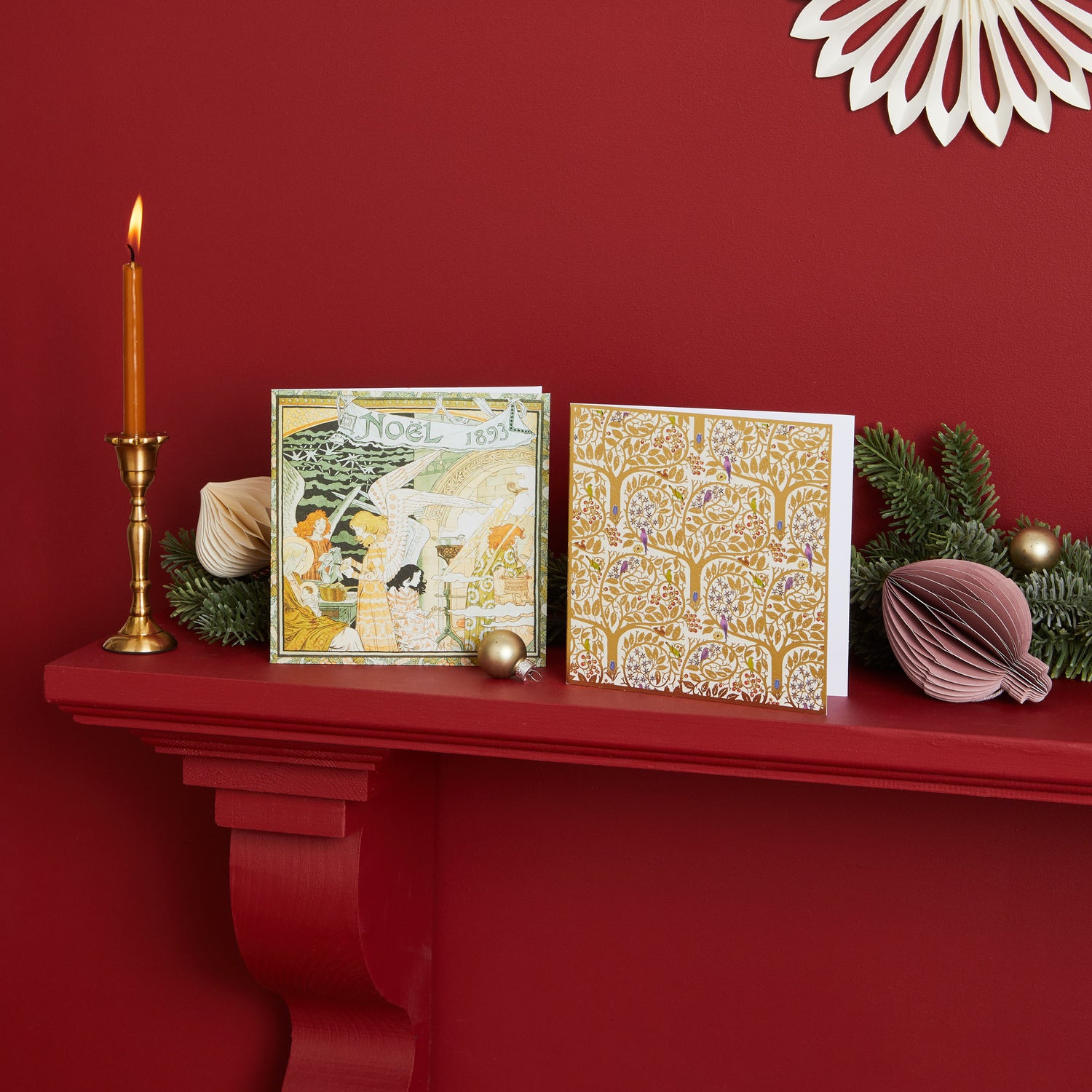 A deep red painted mantlepiece with a candle stick and candle and who Shelter Christmas cards surrounded by festive decorations.