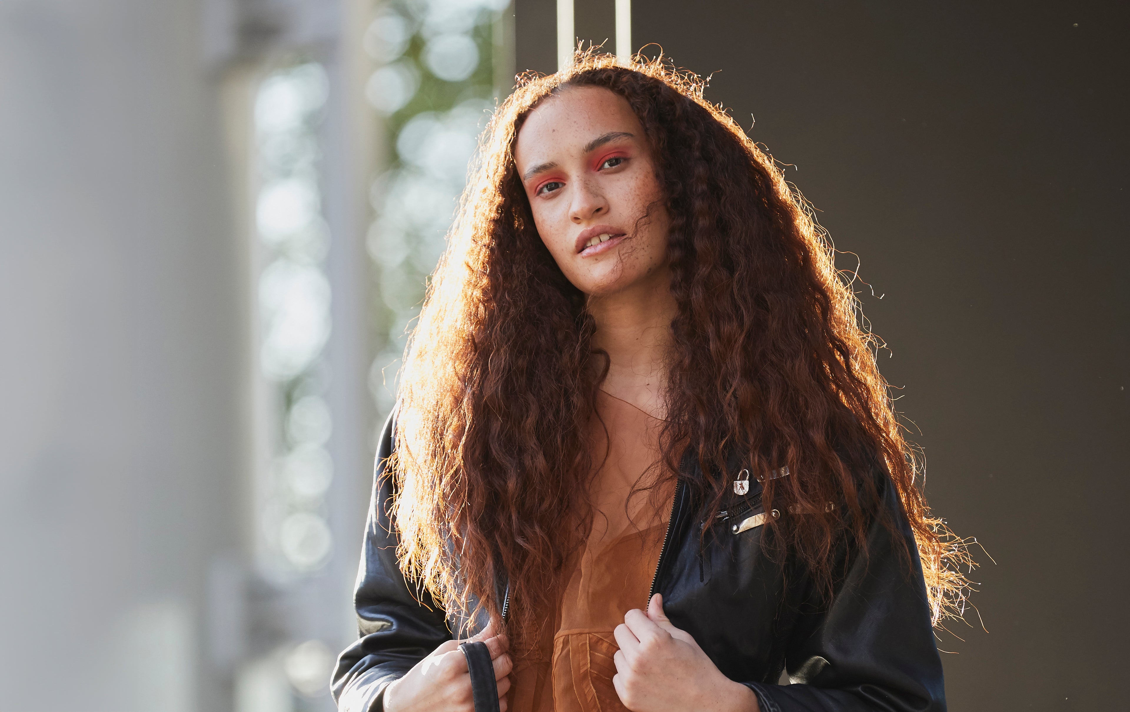 Head / shoulders photo of a model wearing a black leather jacket over an orange dress.