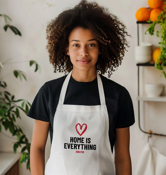 Photo of woman wearing a white apron with a red heart design and bold black lettering that reads 'HOME IS EVERYTHING'