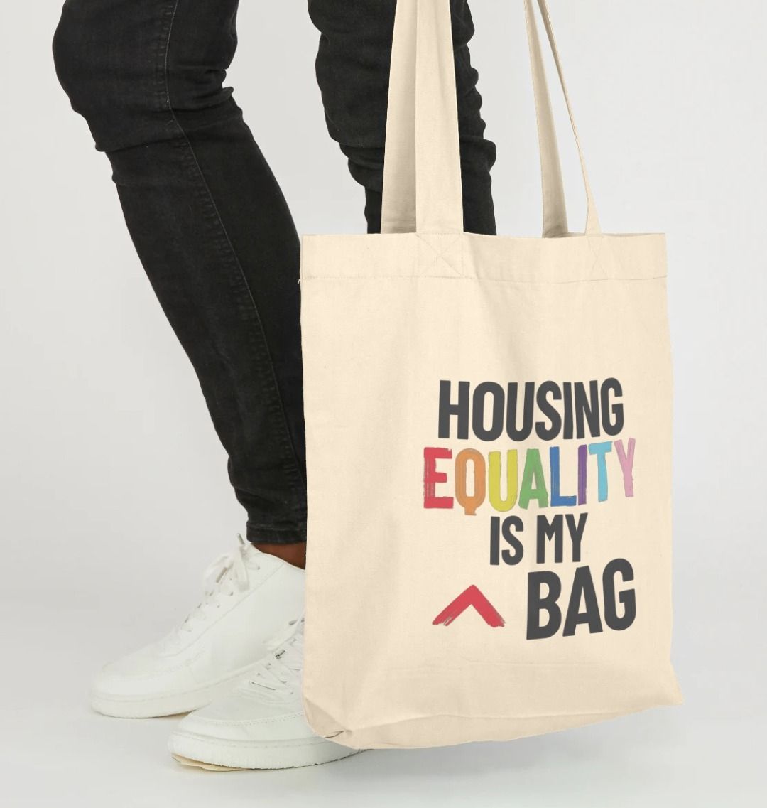 natural canvas colour tote bag with bold slogan "housing equality is my bag" the word equality is in the LGBTQ+ flag colours and the rest of text in black bold lettering