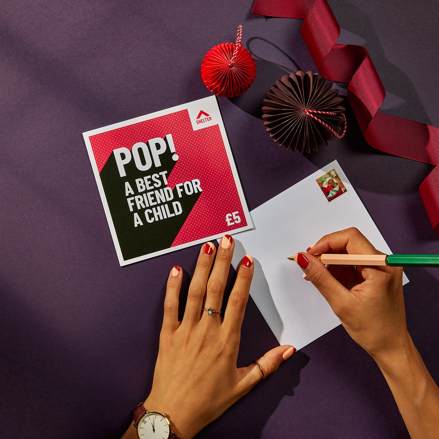 image shows an envelope being written. the envelope is next to a shelter charity gift card. the card is read and has text that reads 'pop! a best friend for a child £5'