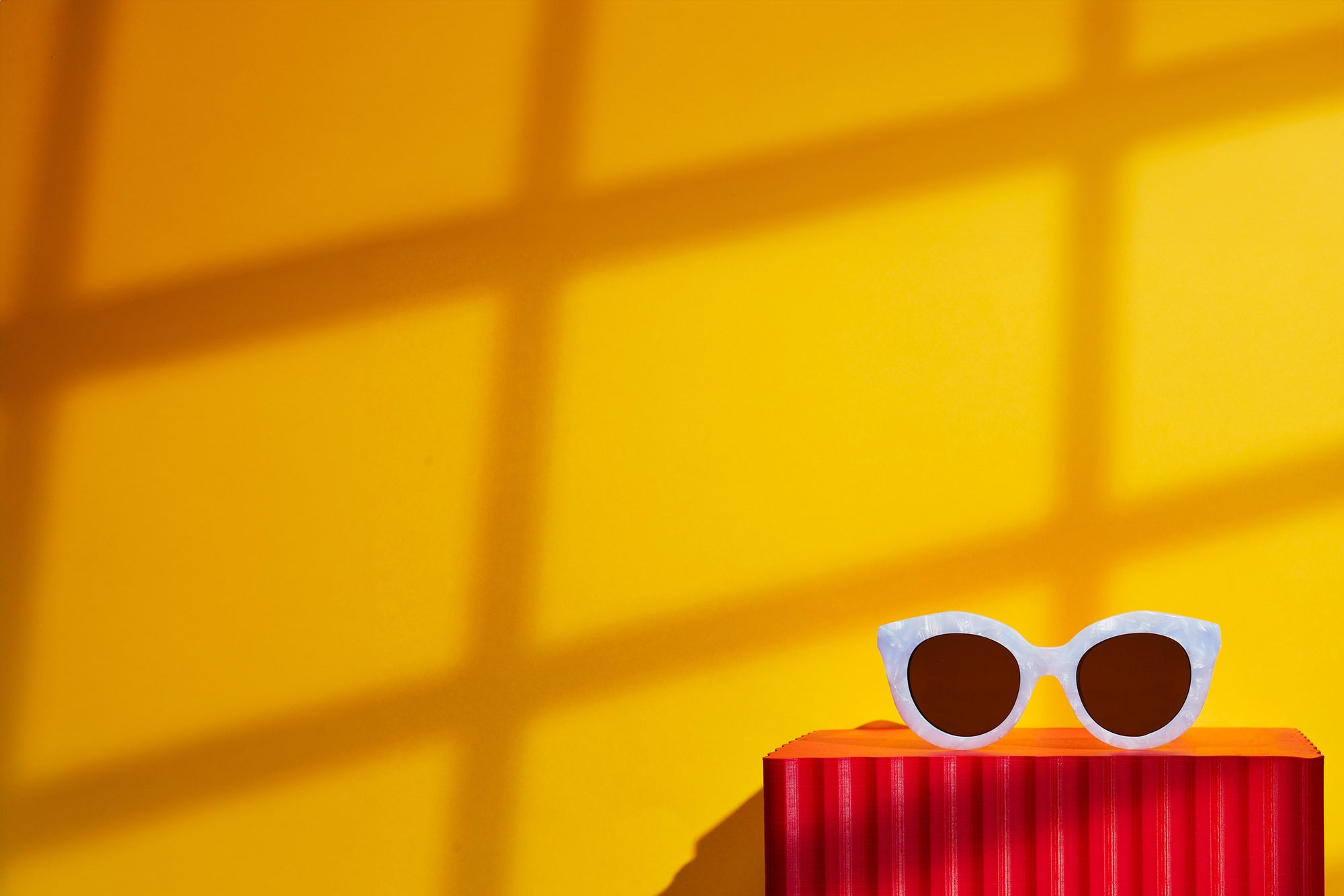 A pair of white cat eye sunglasses sat on a red box against a yellow background